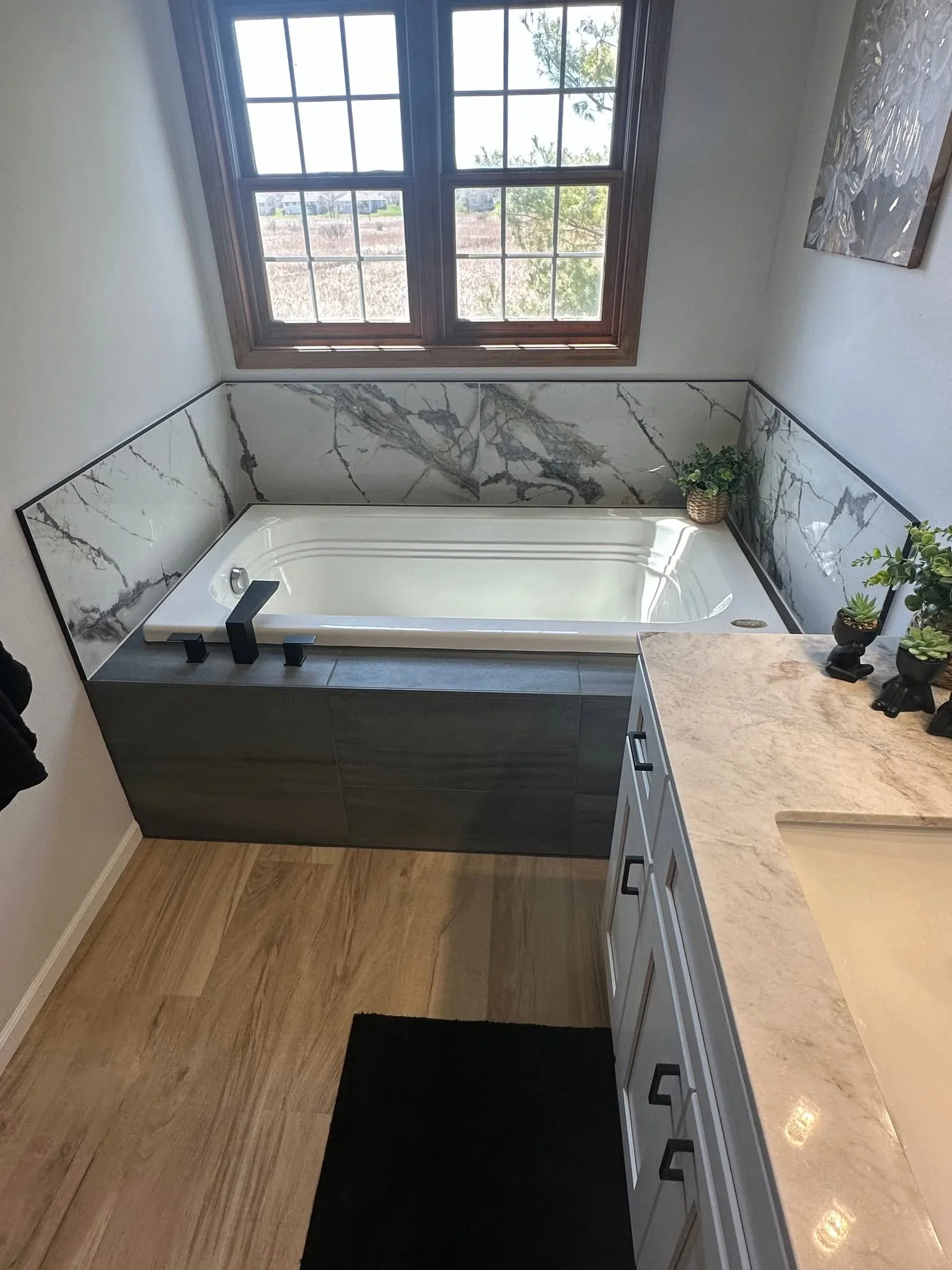 Freestanding soaking tub with marble tile surround, black fixtures, and marble countertops in renovated bathroom