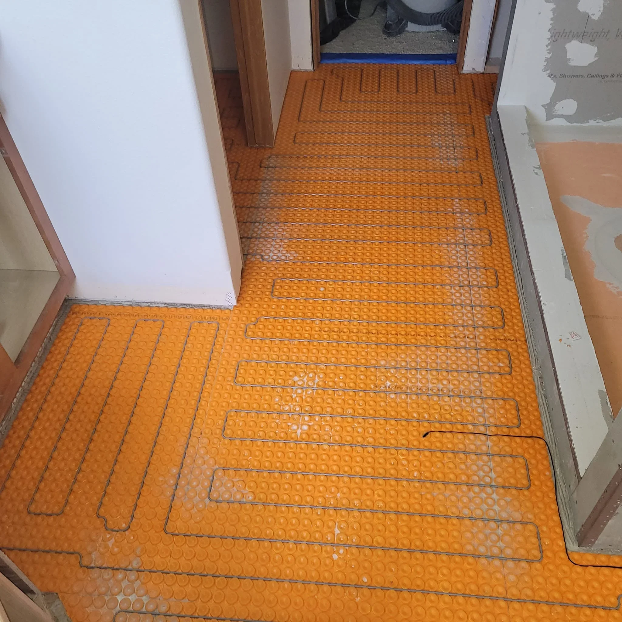 Orange radiant floor heating mat with tubing loops on subfloor before tile installation