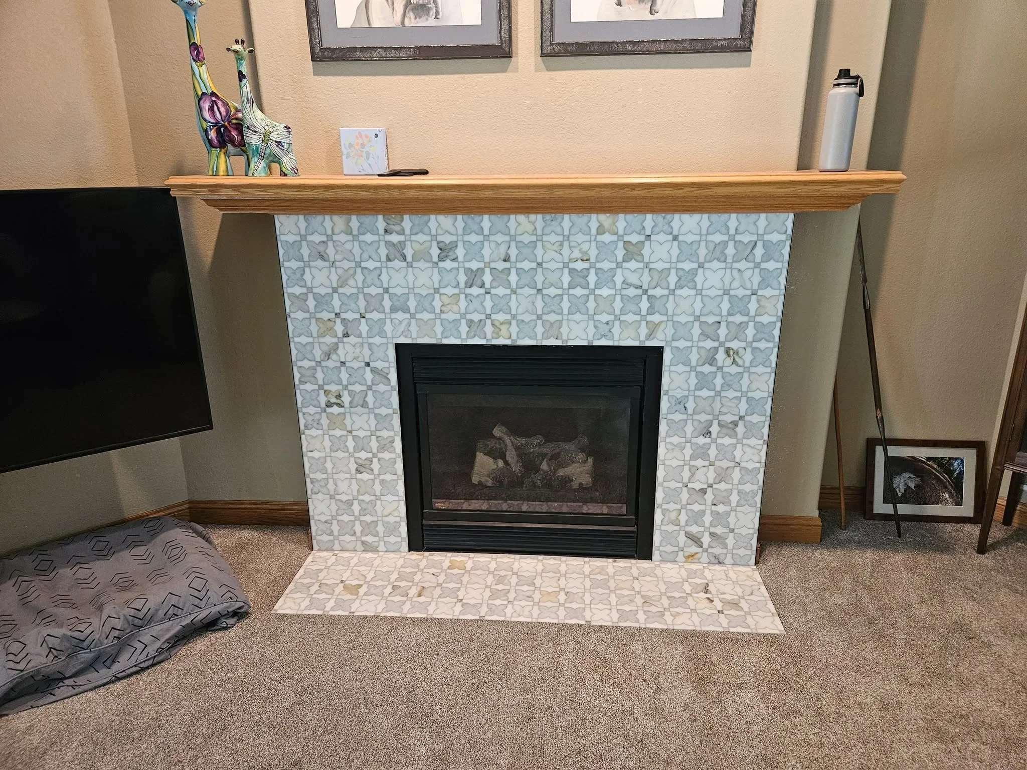 Light blue and gray marble mosaic tile fireplace surround with black insert and wood mantel