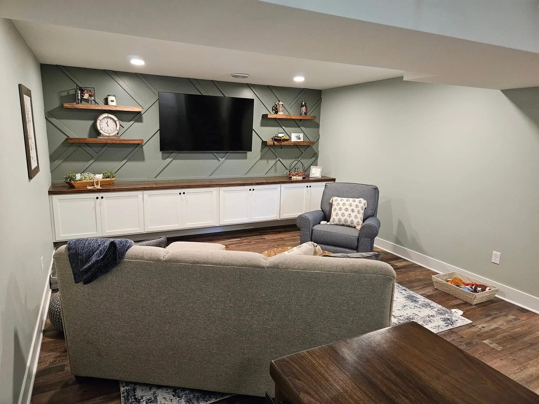 Custom white cabinetry with dark wood countertop, diagonal shiplap wall, and floating shelves in basement media room