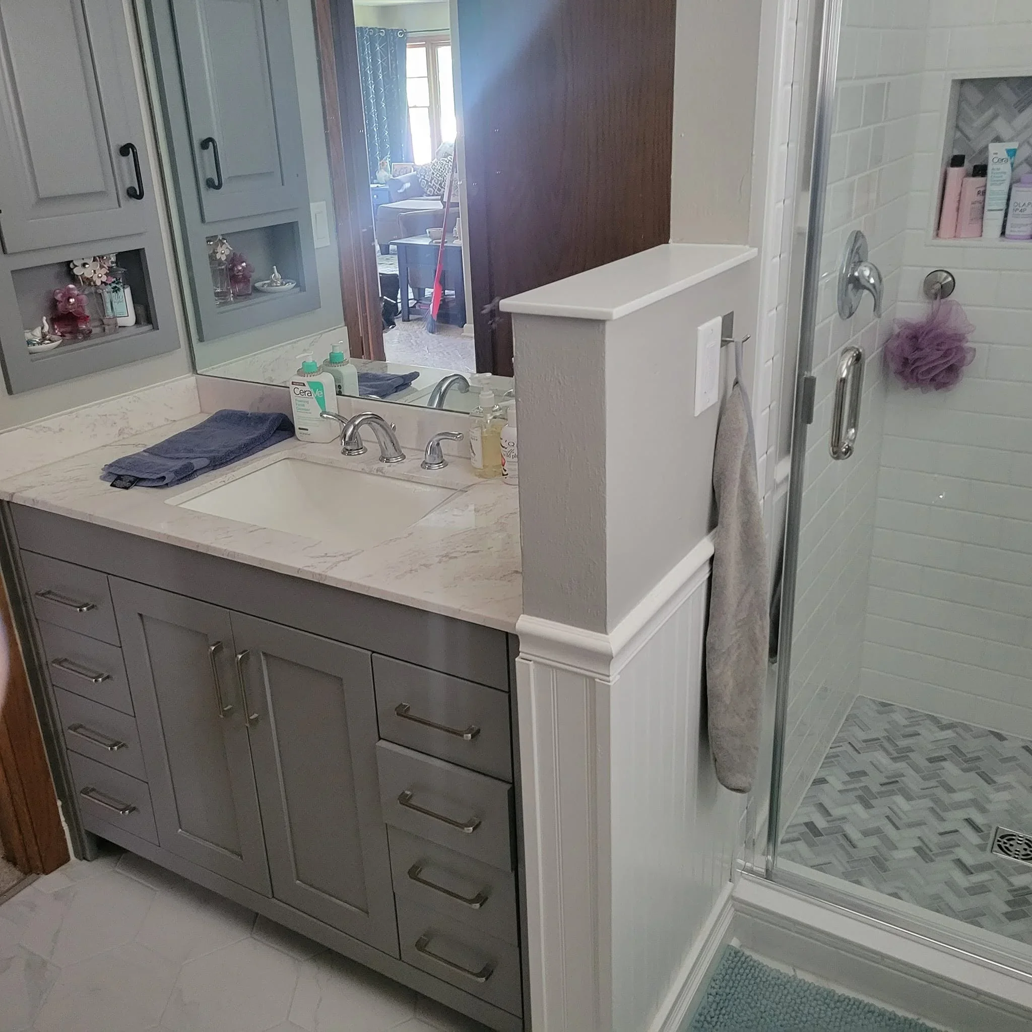 Gray vanity with marble countertop, chrome faucet, and walk-in shower with herringbone tile flooring