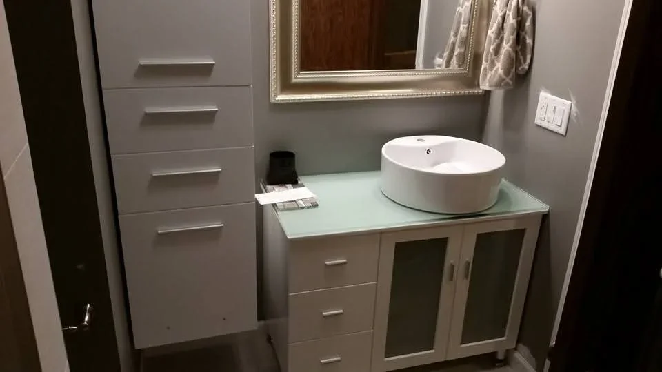 White bathroom vanity with vessel sink, glass countertop, and framed mirror