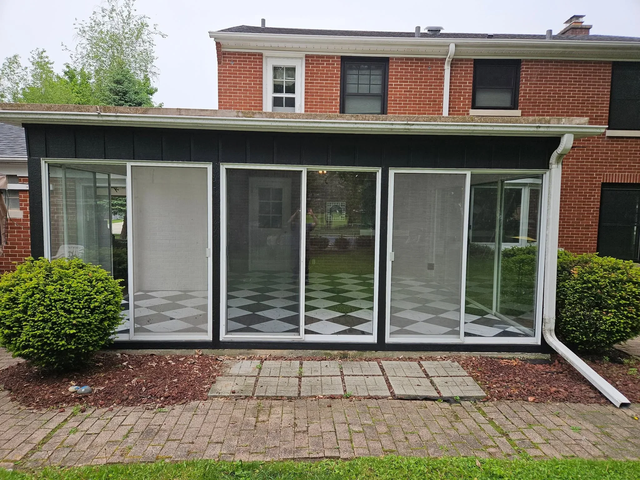Sunroom with white-framed sliding glass doors and black trim attached to brick home