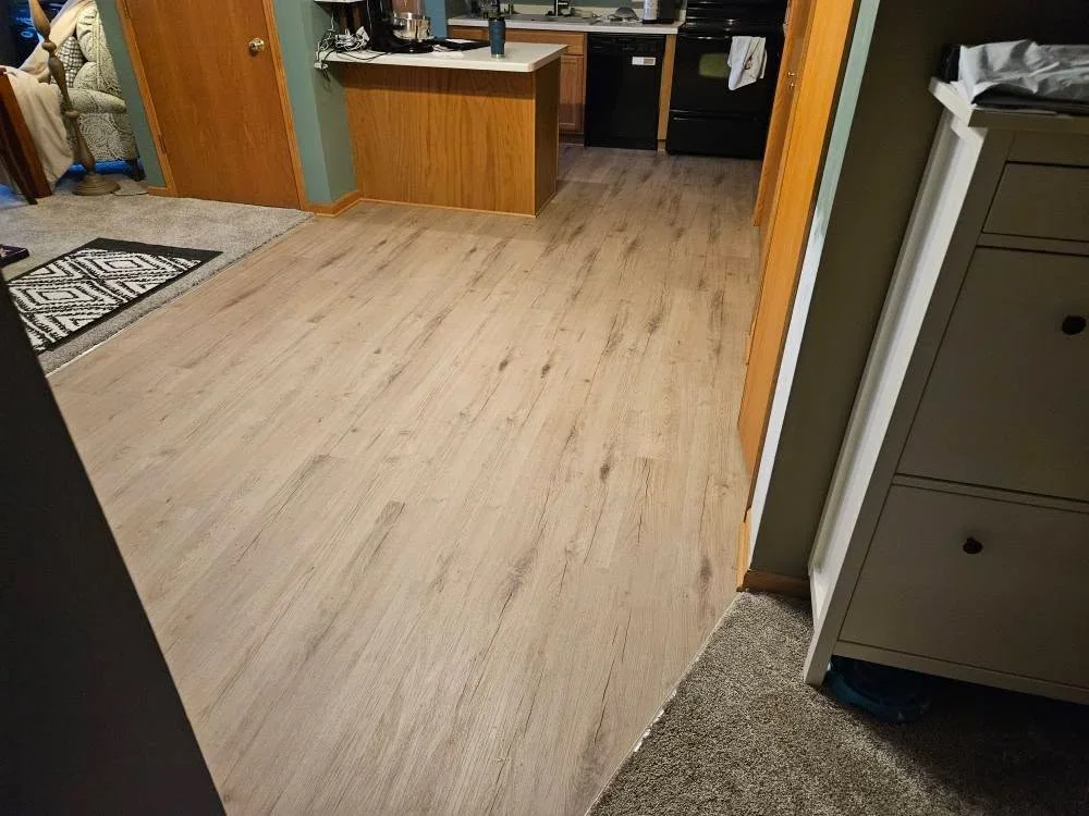 Light oak luxury vinyl plank flooring installed in kitchen with wood cabinetry and transitions to adjacent rooms