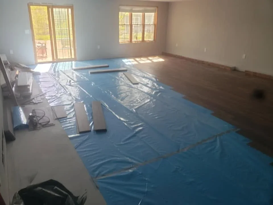 Hardwood flooring installation with protective sheeting and finished dark wood flooring in open room
