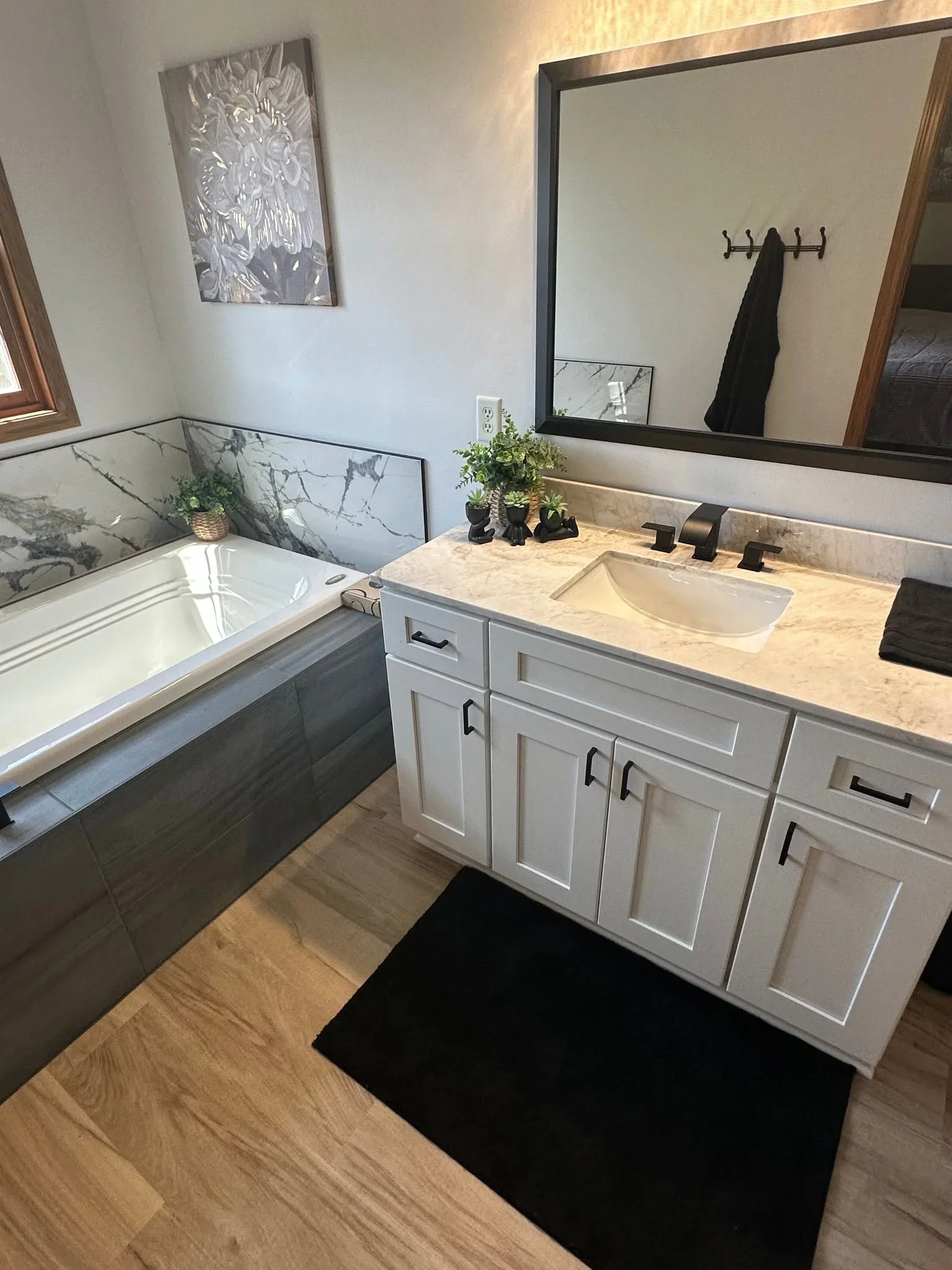 White vanity with marble countertop, vessel sink, and soaking tub with marble tile surround