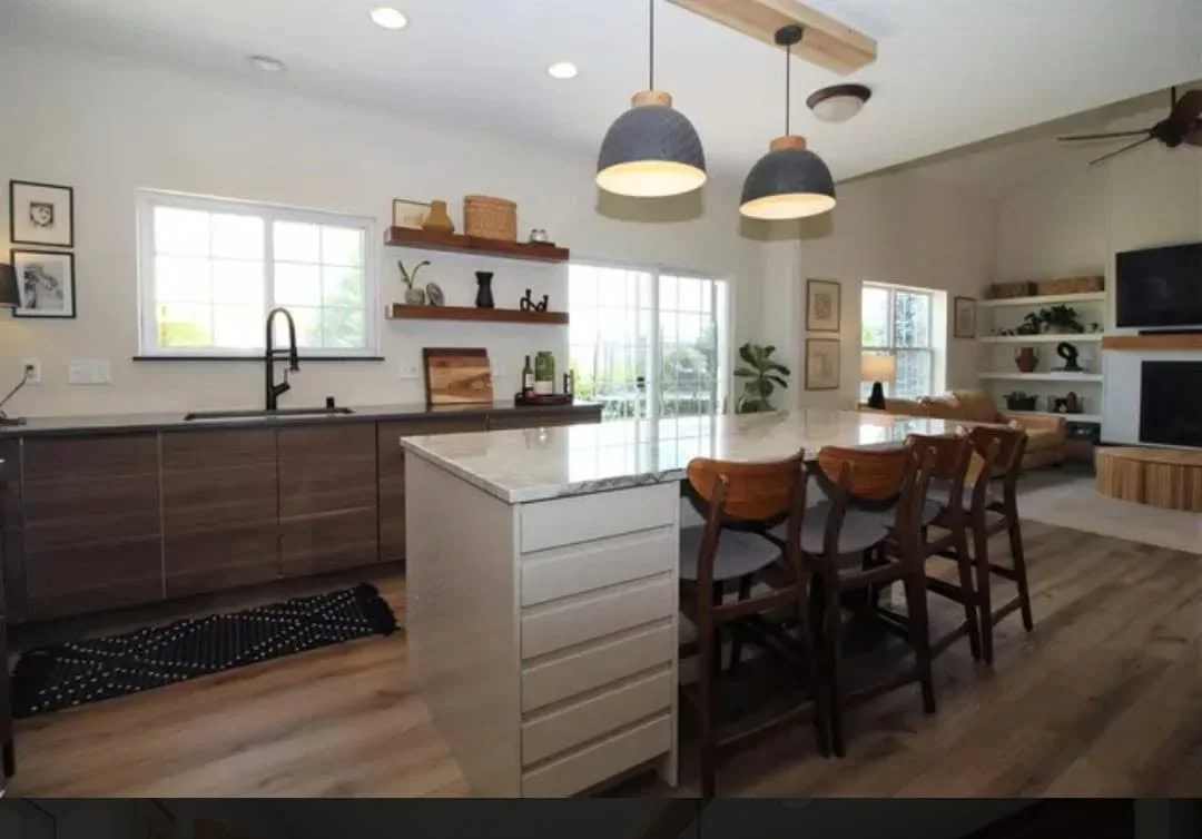Modern kitchen with dark cabinets, white island, floating shelves, pendant lights, and hardwood floors
