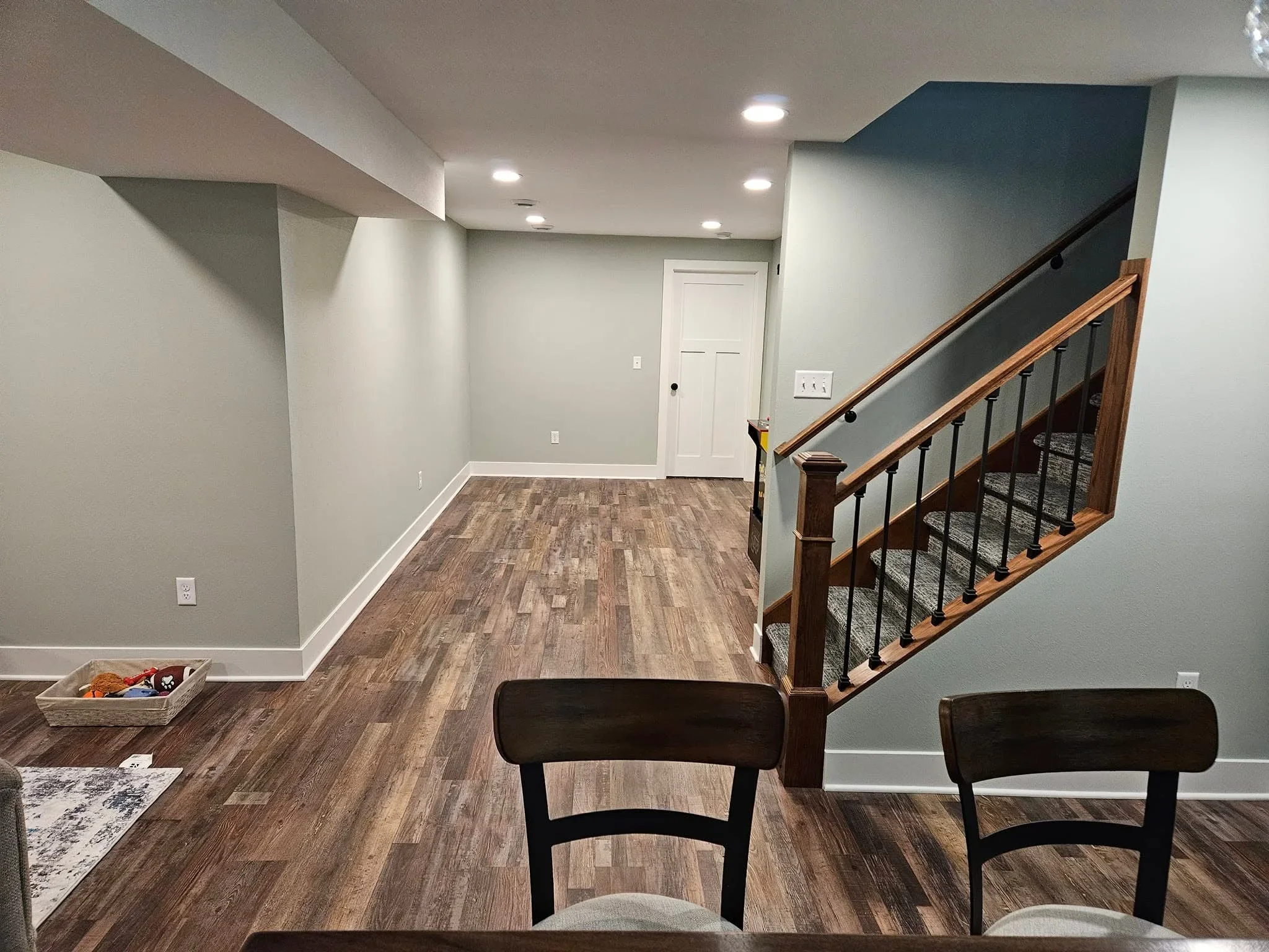 Finished basement with luxury vinyl plank flooring, gray walls, recessed lighting, and wood stair railing