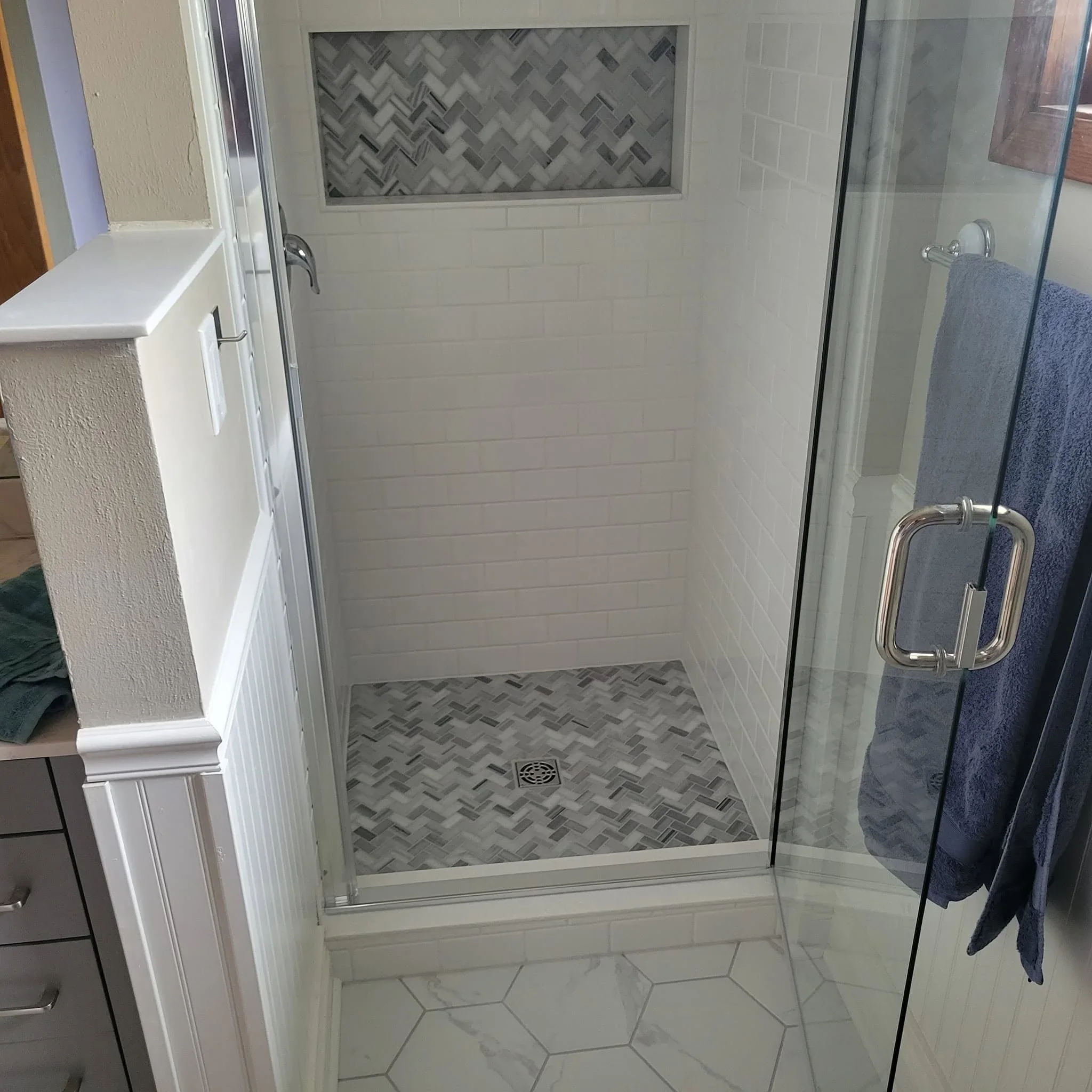 Frameless glass shower with subway tile walls and herringbone tile floor and niche