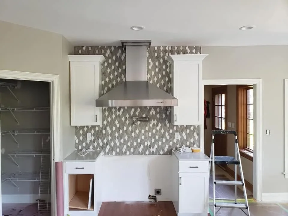 White kitchen cabinets with gray diamond tile backsplash and stainless steel range hood