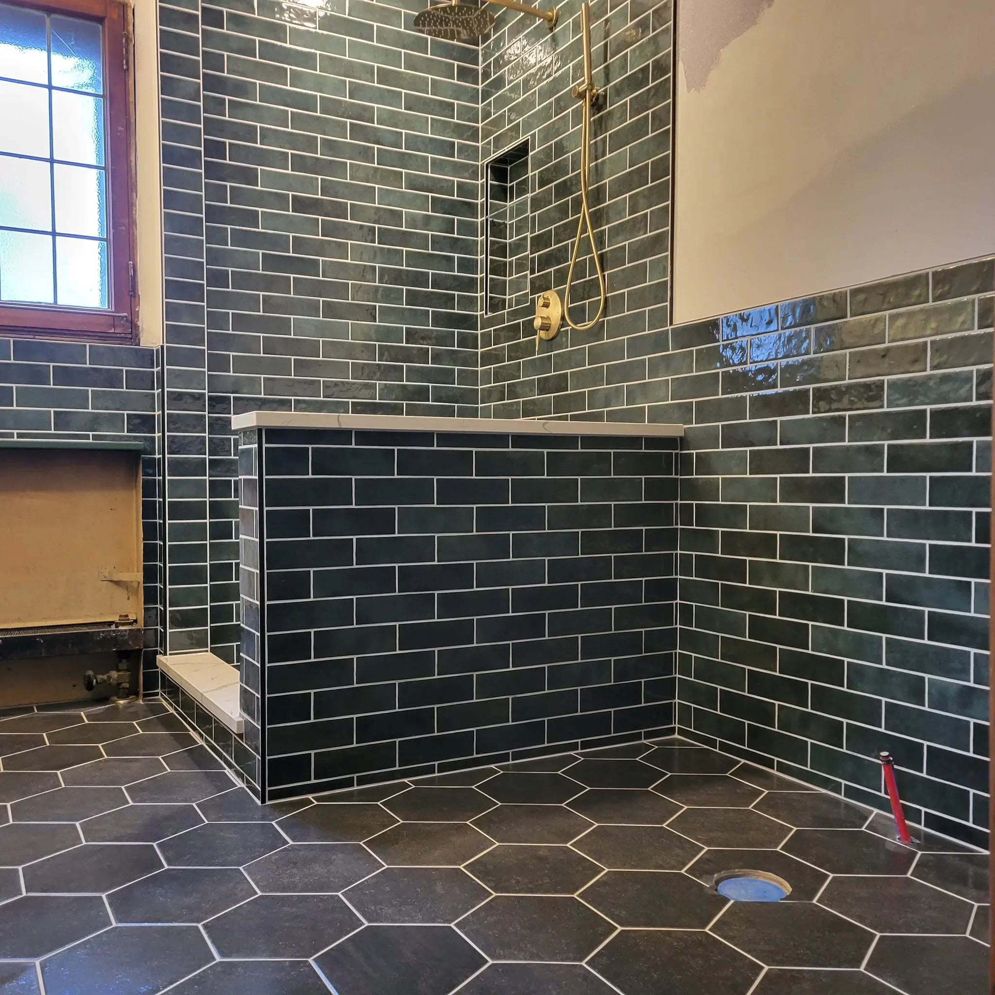 Dark green subway tile shower walls with hexagonal charcoal floor tile and brass fixtures