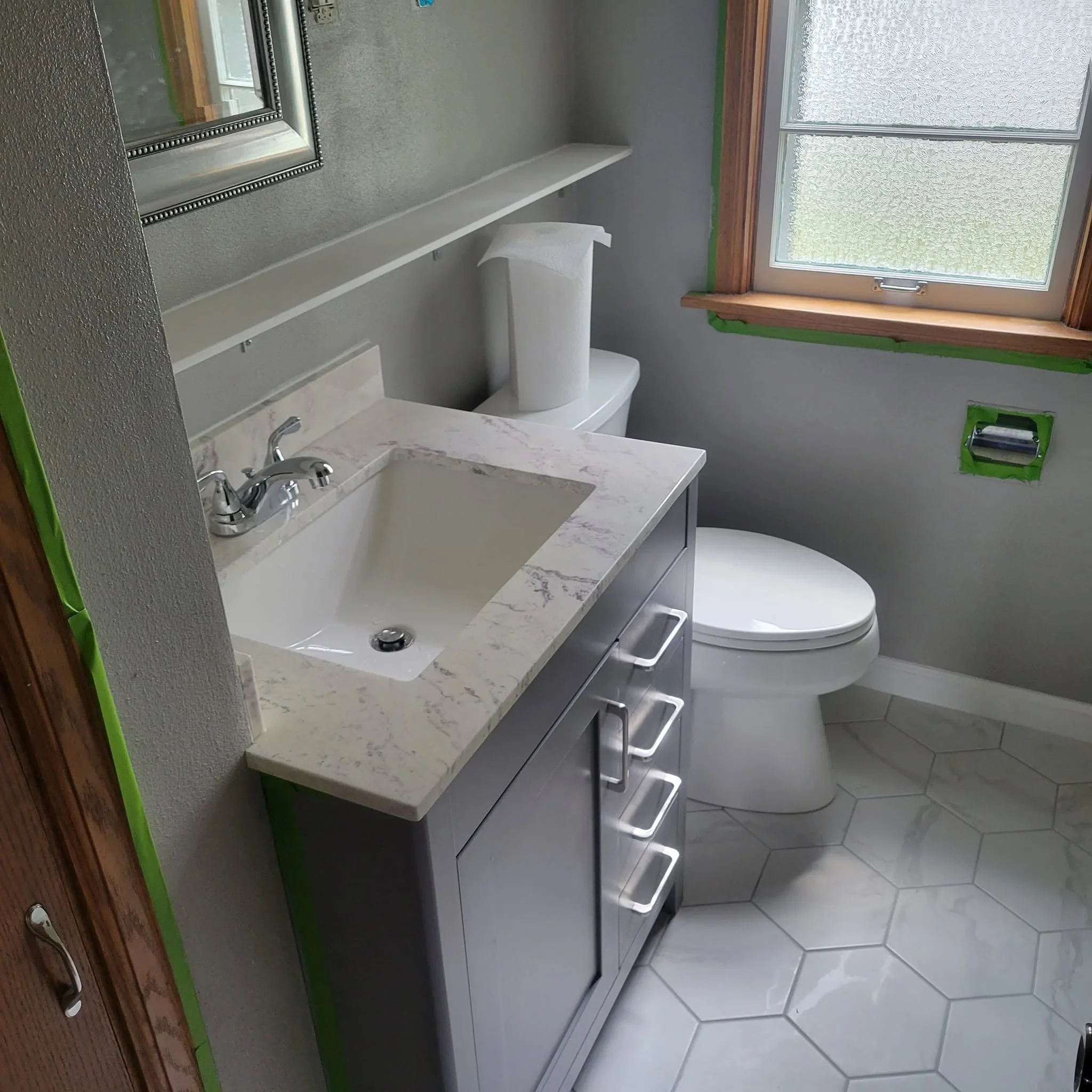 Marble countertop vanity with undermount sink, chrome faucet, and white hexagonal floor tile