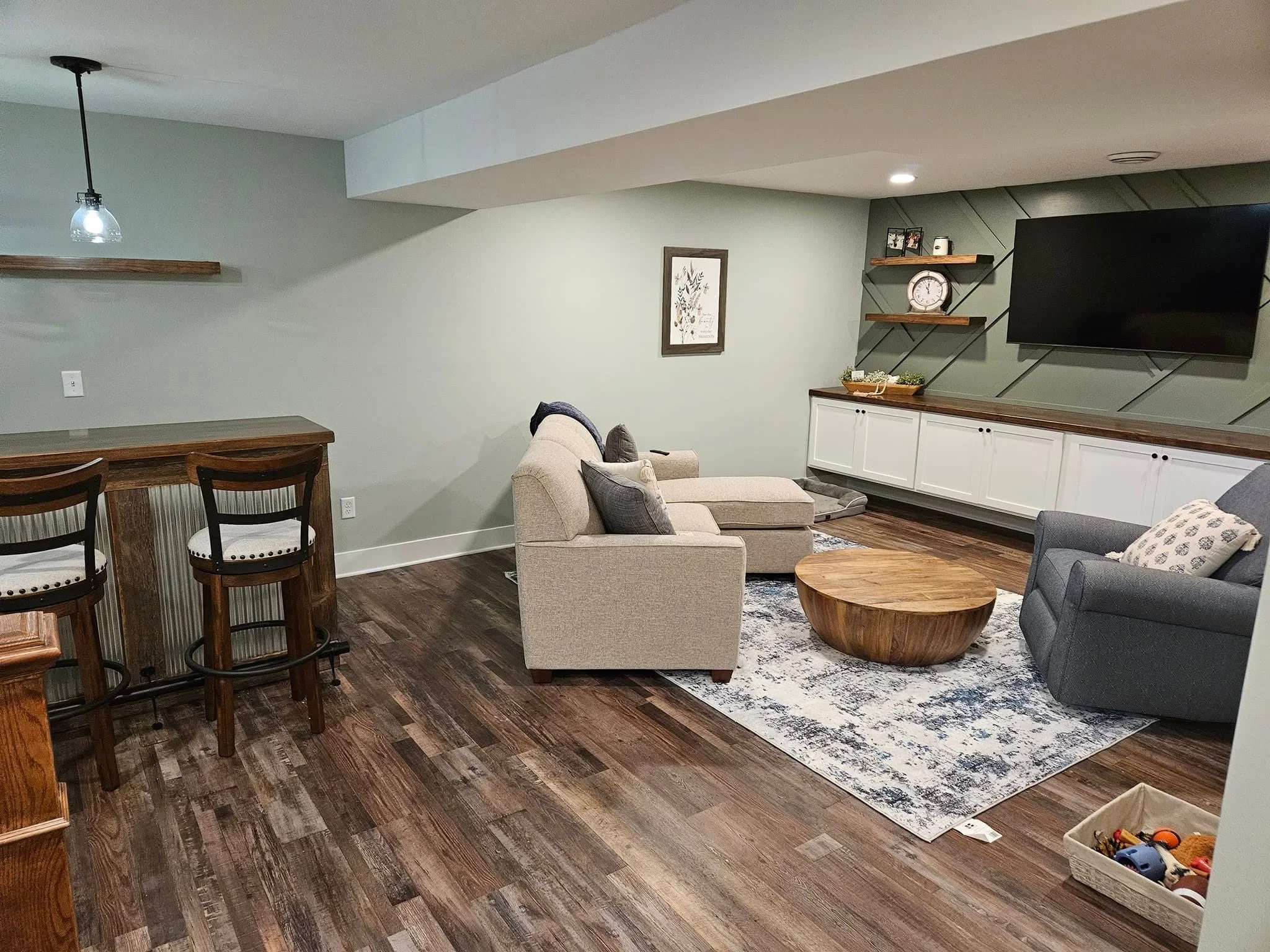 Finished basement with hardwood flooring, white cabinetry, floating shelves, and seating area