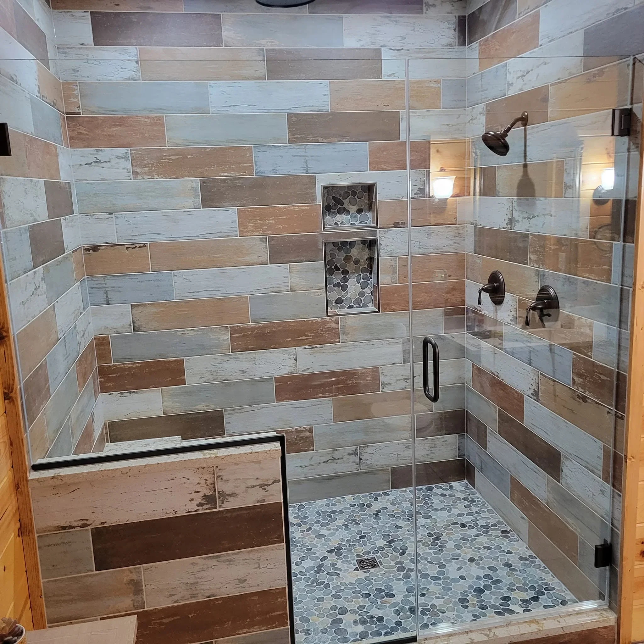 Tiled shower with wood-look planks, hexagonal floor tiles, glass enclosure, and built-in niches