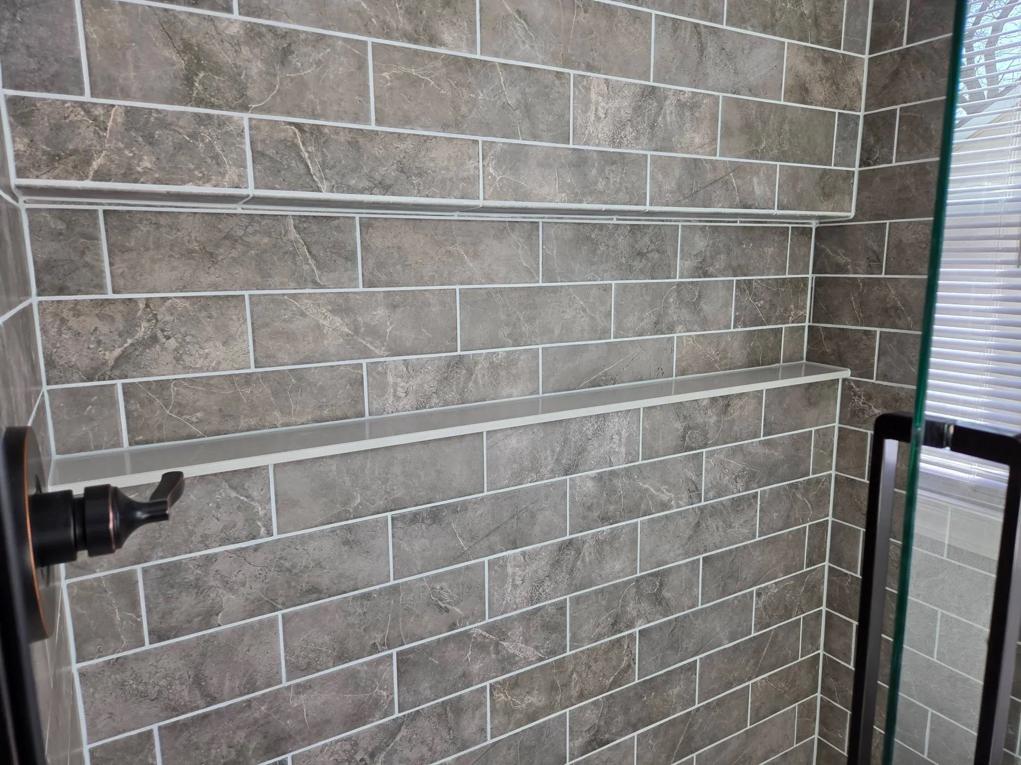 Gray subway tile shower with white grout, chrome shelf and fixtures