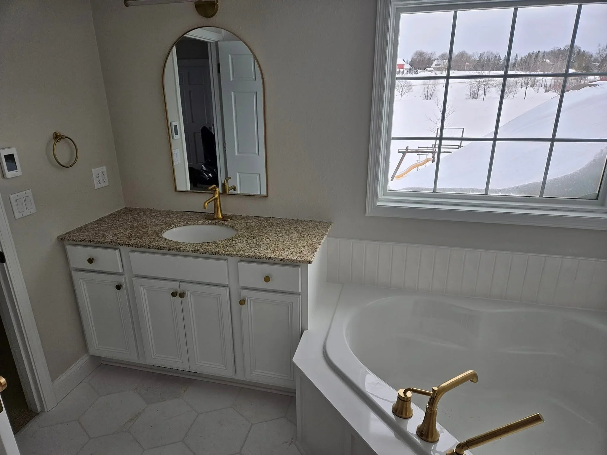 White vanity with granite countertop, brass faucet, and soaking tub with hexagonal tile flooring