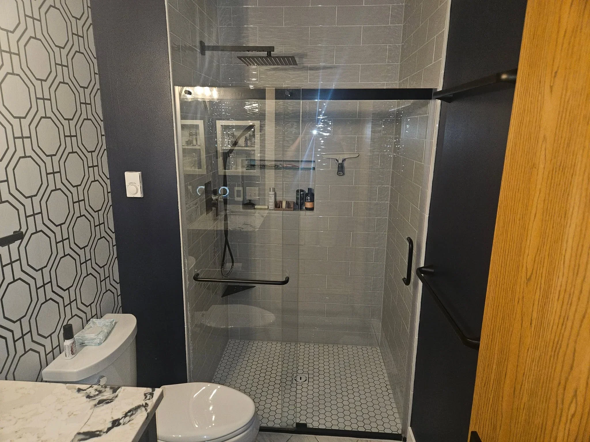 Walk-in shower with gray subway tile, hexagonal floor tile, frameless glass enclosure, and black fixtures