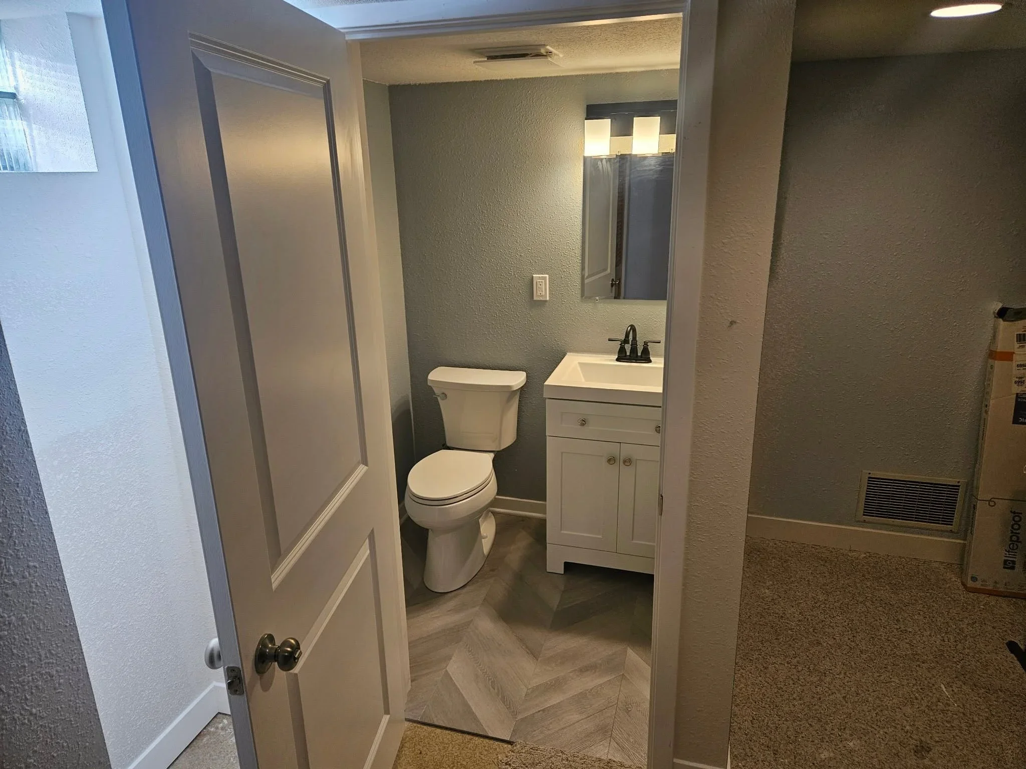 Renovated bathroom with white vanity, toilet, textured walls, and vinyl plank flooring