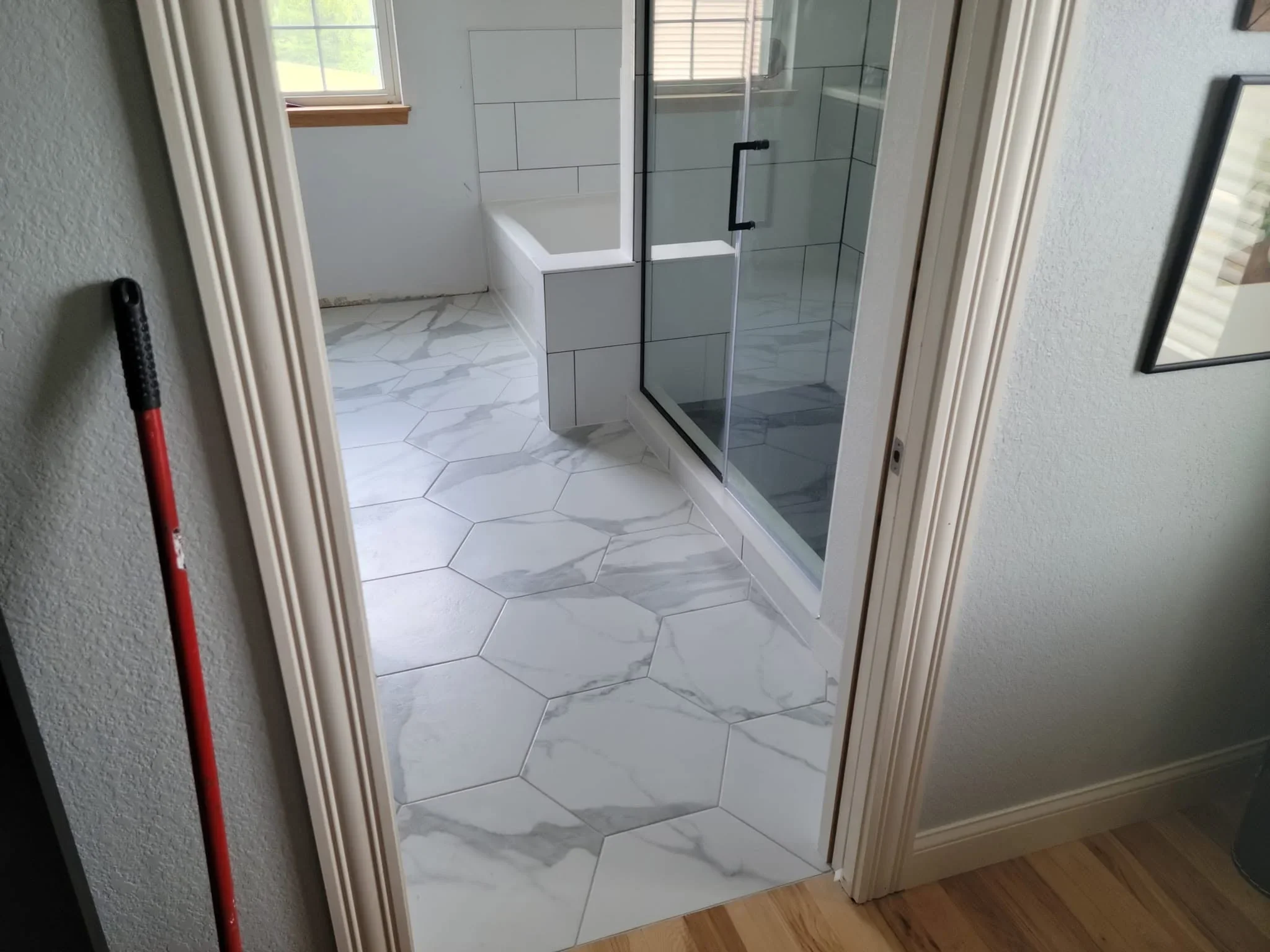 Hexagonal marble-look tile flooring, frameless glass shower, white subway tile walls, freestanding tub