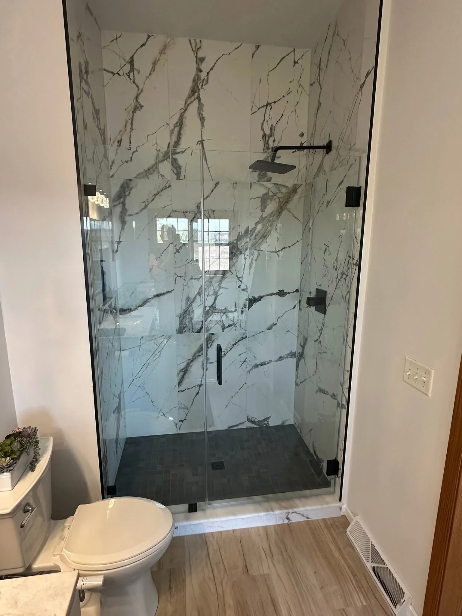 Frameless glass shower with white and gray marble tile walls and dark floor tile