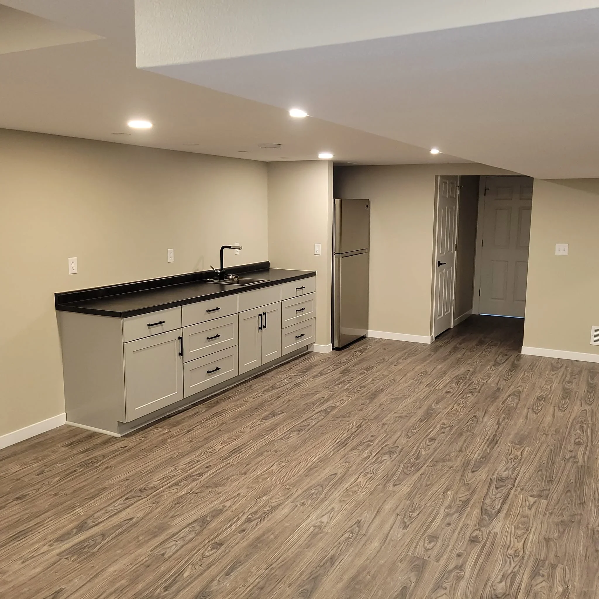 Custom cream cabinetry with black countertop, sink, and matte black faucet in finished basement space