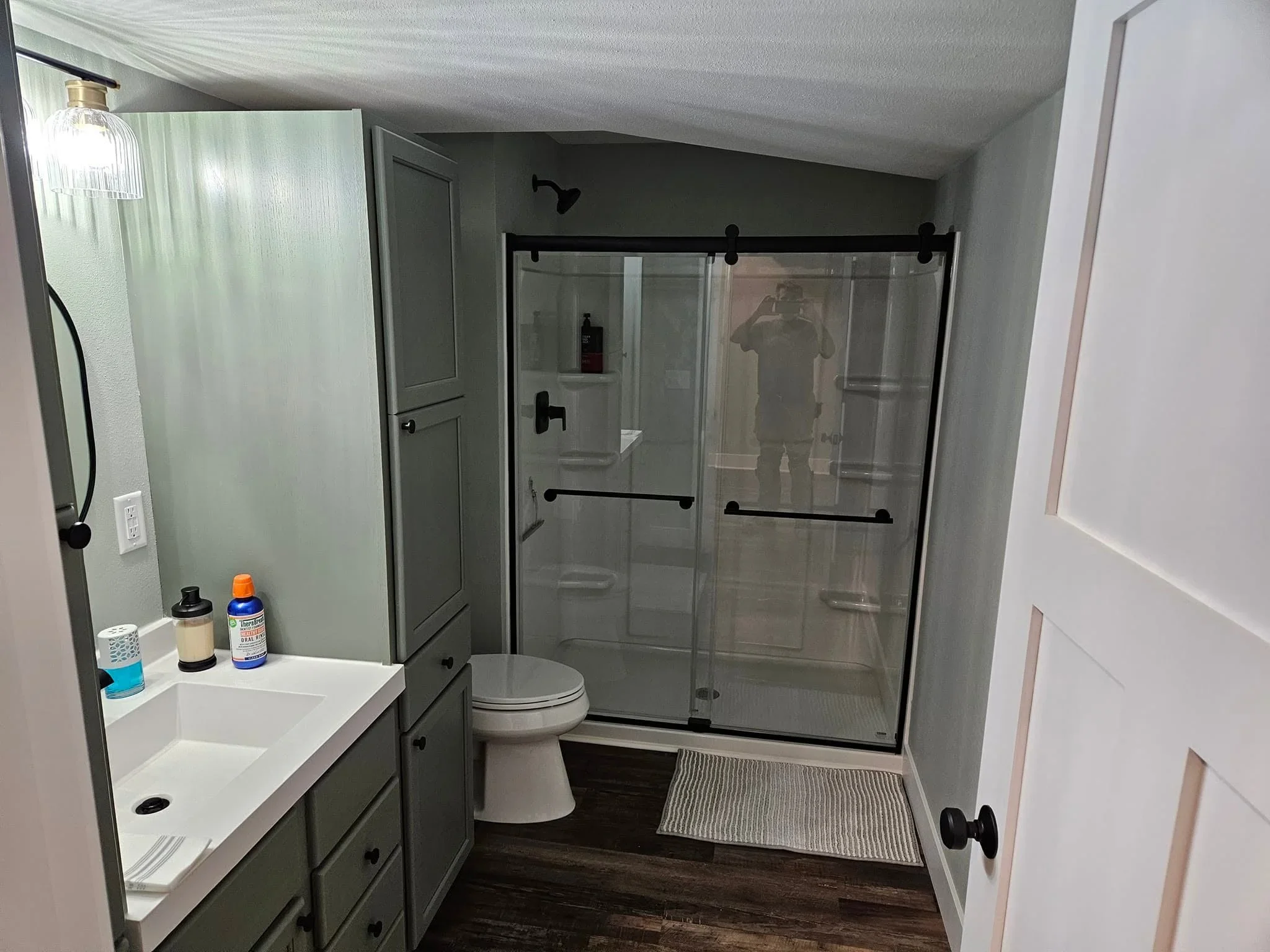 Bathroom with gray vanity, white quartz countertop, frameless glass shower enclosure, and dark wood flooring