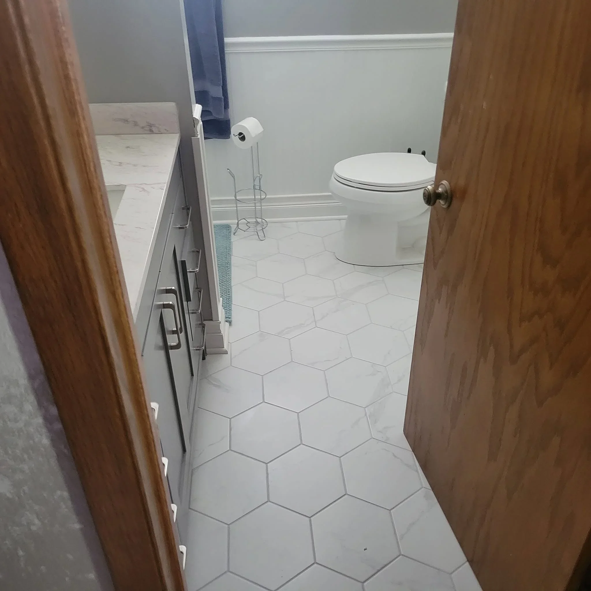 White hexagonal floor tile, painted walls with molding, new porcelain toilet installation