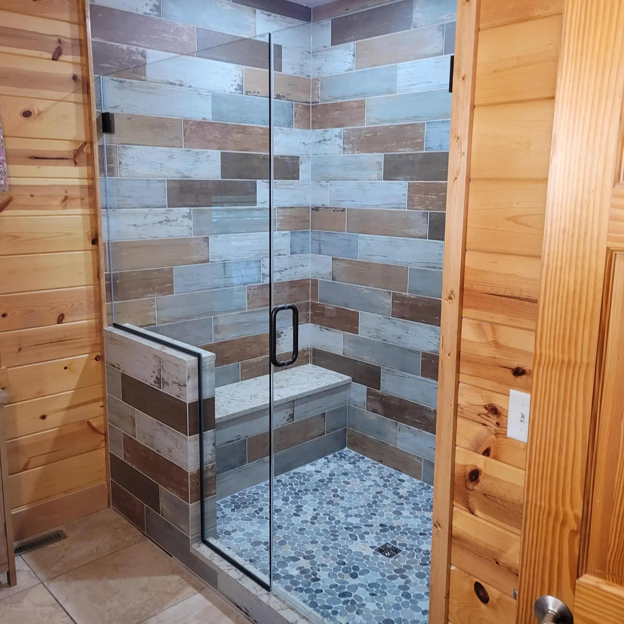 Walk-in shower with mixed wood-look tile, pebble floor, and frameless glass enclosure