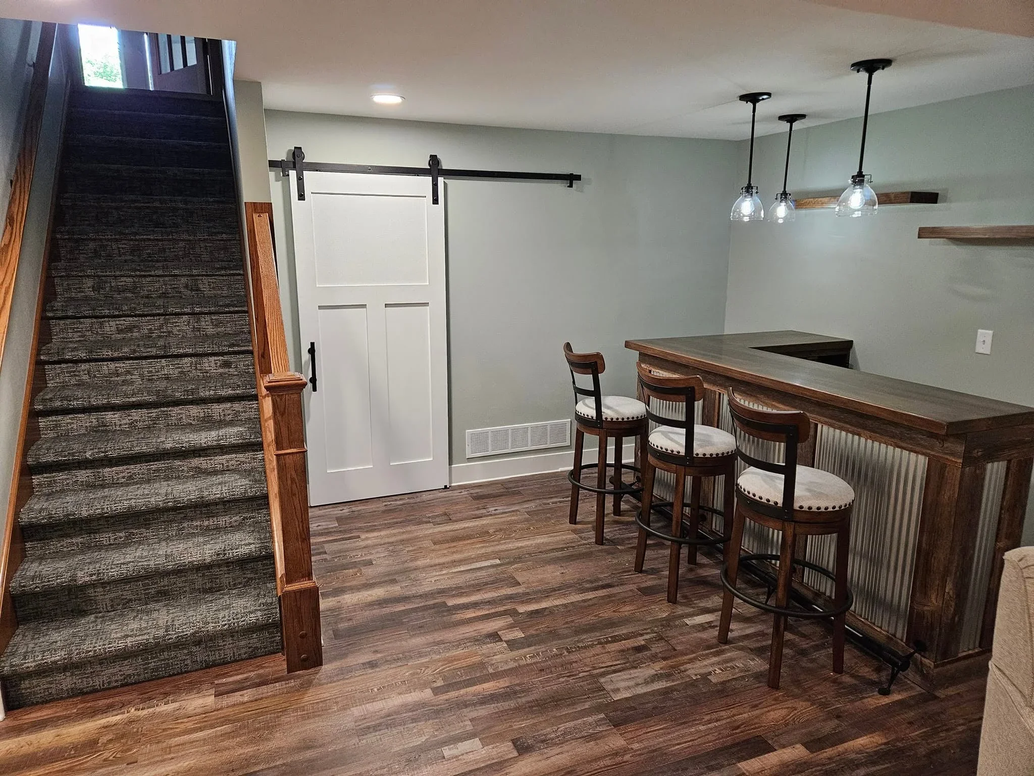 Finished basement bar with wood cabinetry, hardwood floors, and pendant lighting