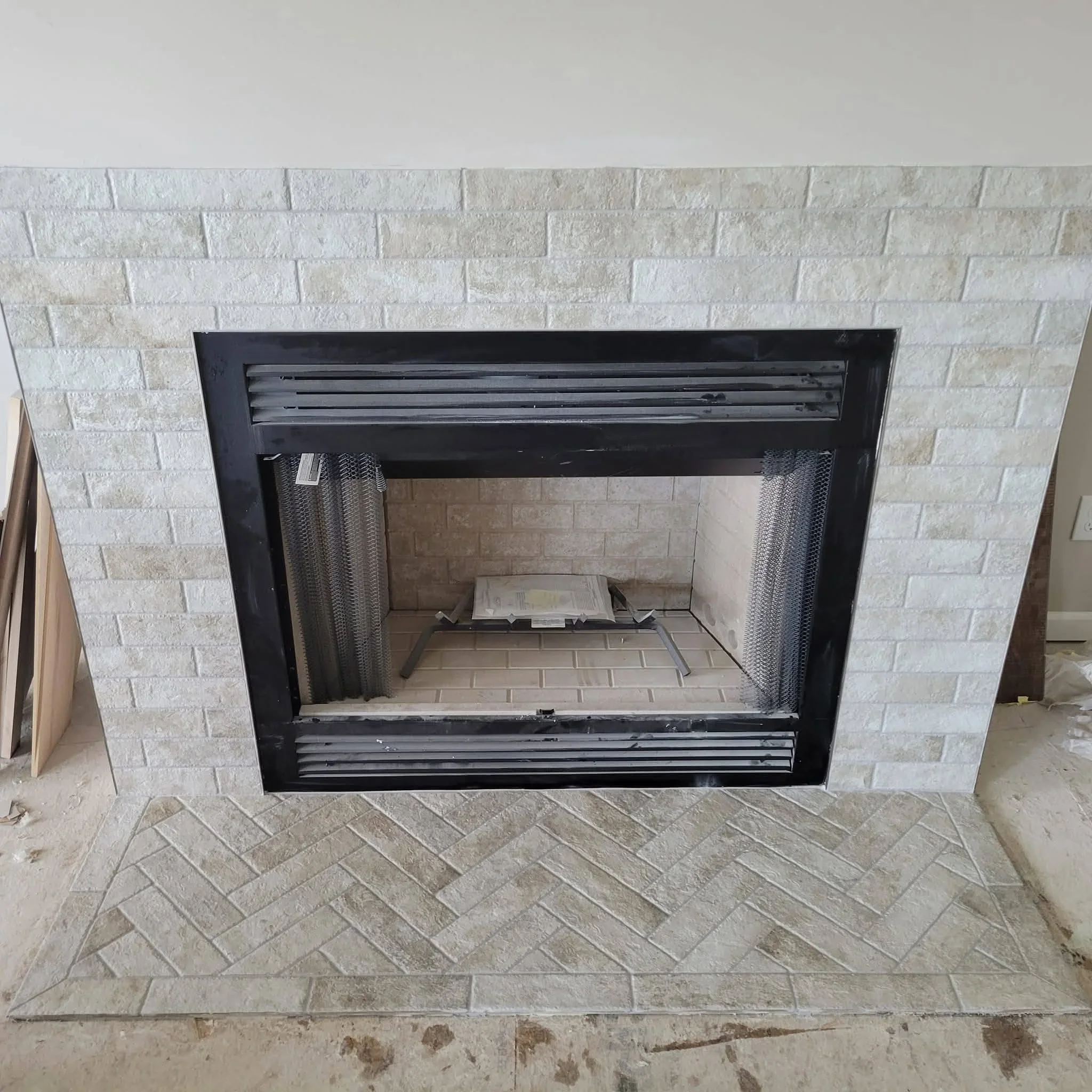 Black fireplace insert with stone surround and herringbone tile hearth installation