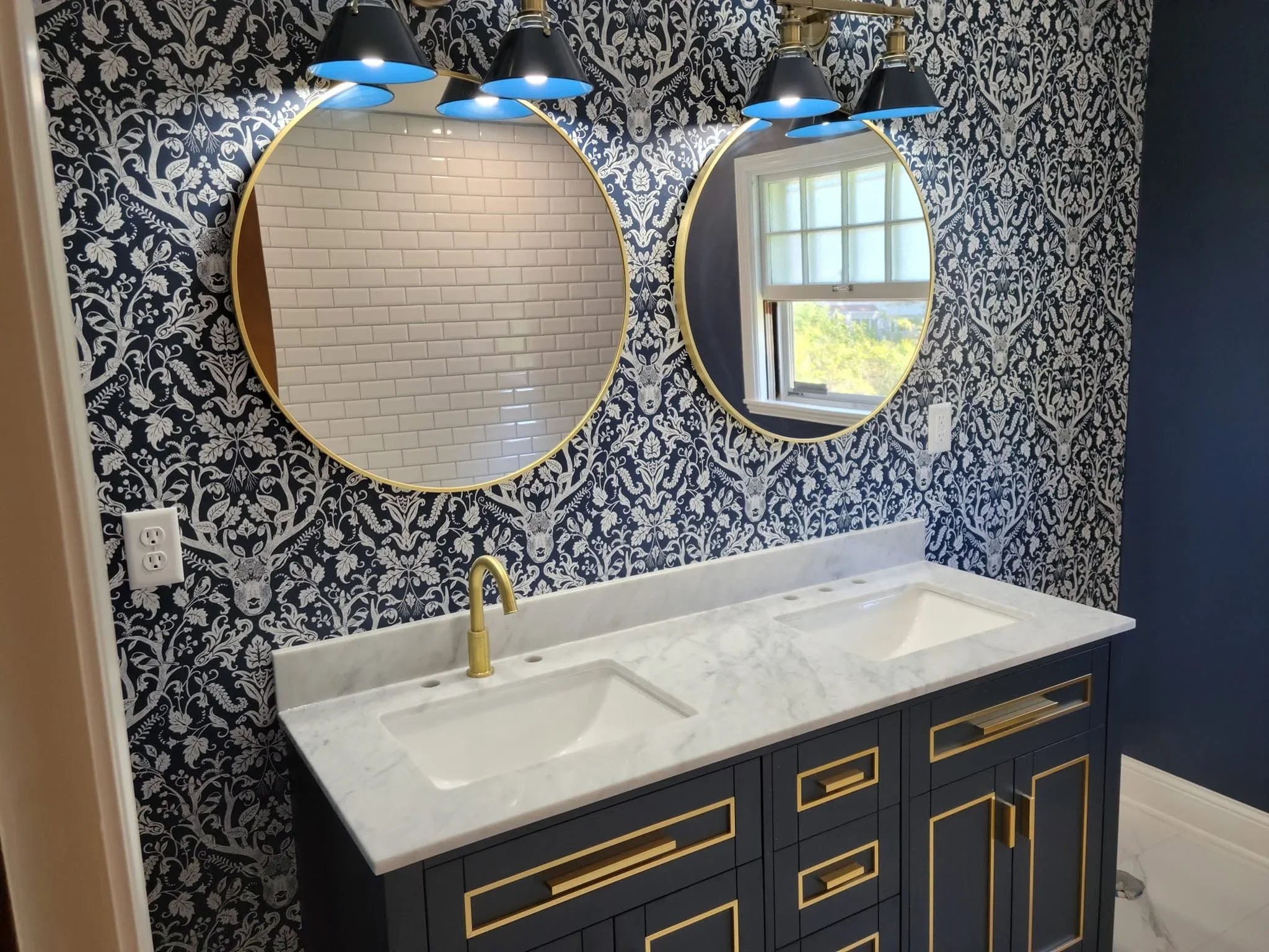 Bathroom vanity with marble countertop, black damask wallpaper, brass mirrors, and pendant lighting