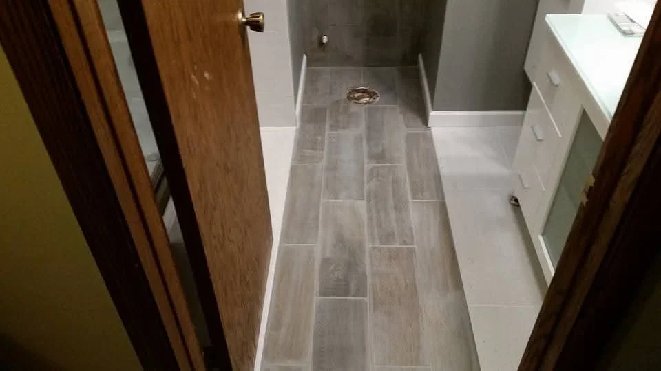Gray wood-look ceramic tile floor in staggered brick pattern with drain opening