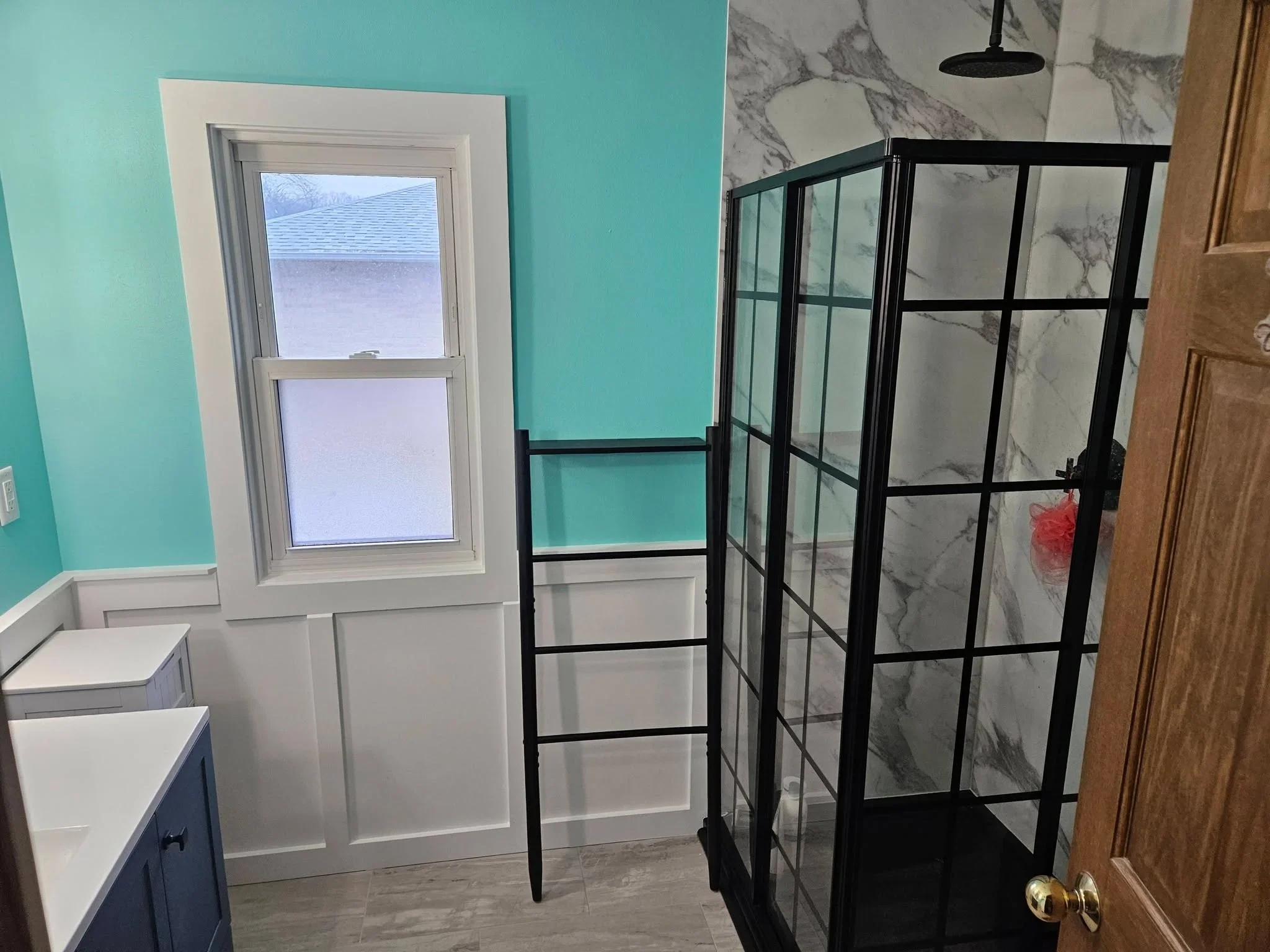 Bathroom with black-framed glass shower, marble tile walls, turquoise paint, and white wainscoting