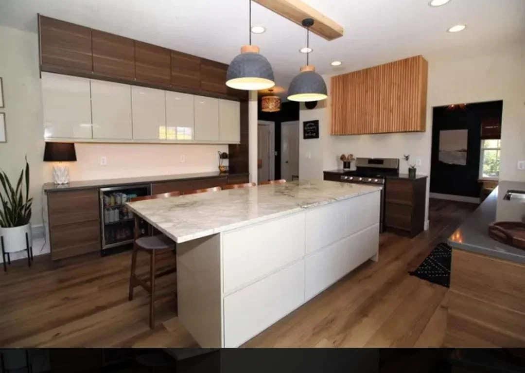 Modern kitchen with white island, marble countertop, two-tone cabinetry, wood accents, and pendant lighting