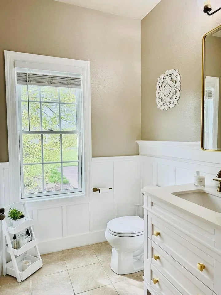 Bathroom with white shiplap wainscoting, white vanity with brass pulls, ceramic tile floor, and large window