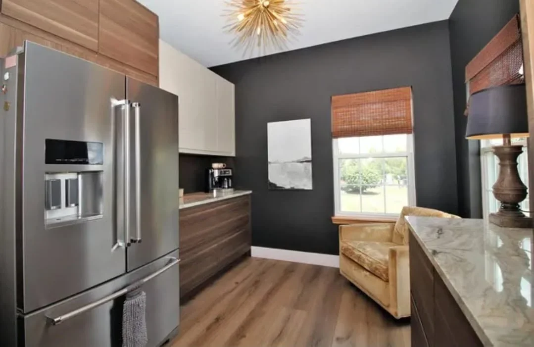 Modern kitchen with two-tone wood and cream cabinetry, stainless steel appliances, marble island, and charcoal accent wall