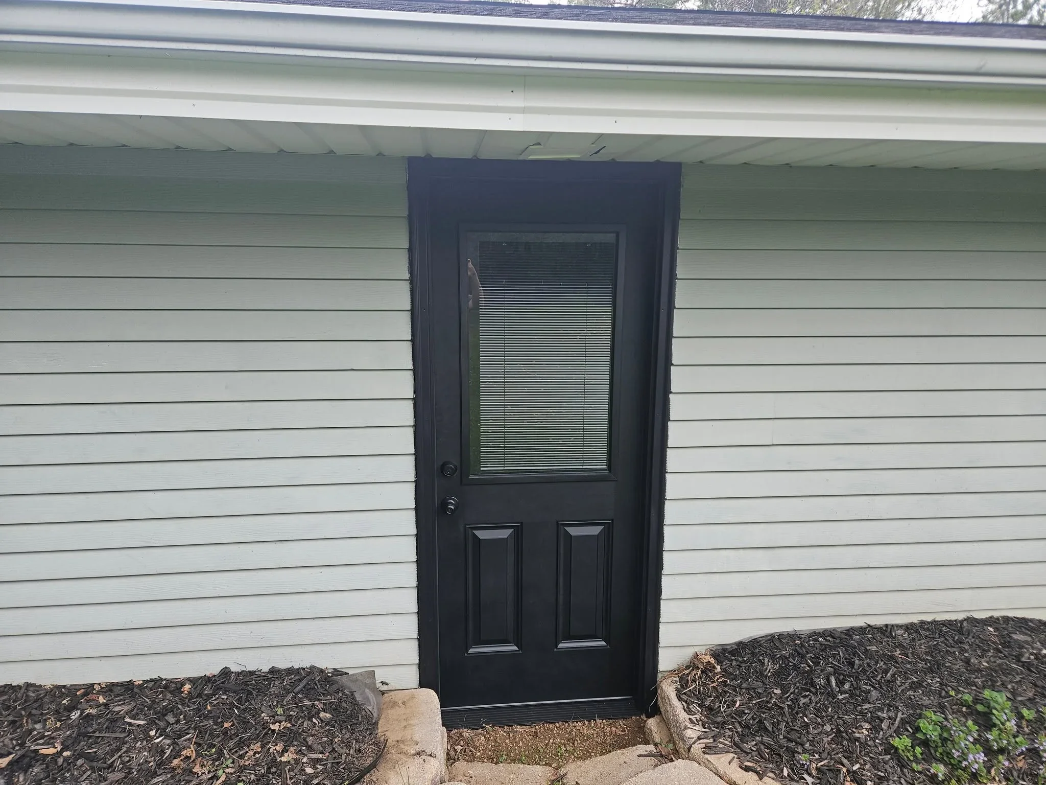 Black entry door with glass panel and blinds on white horizontal siding
