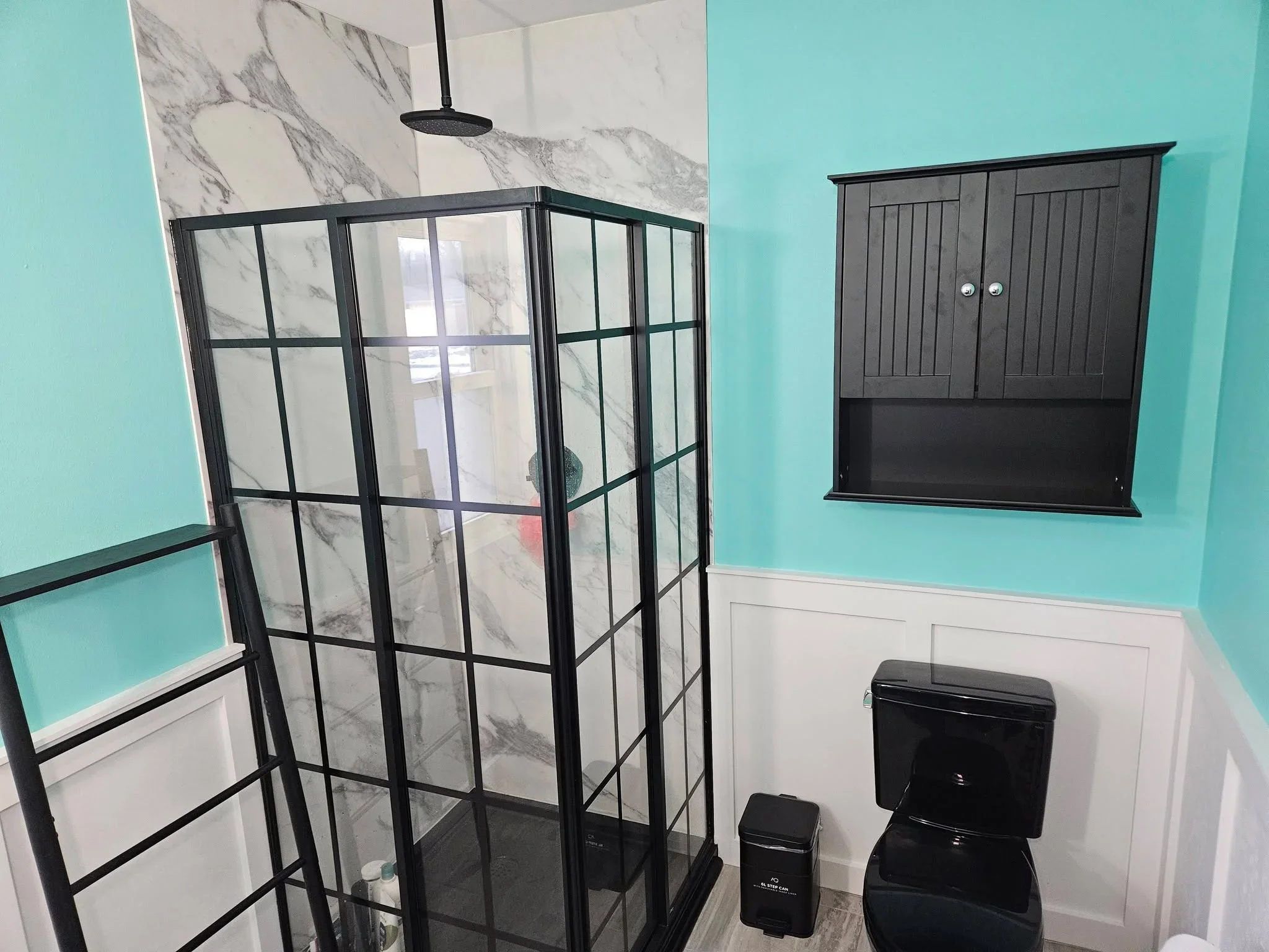 Black-framed glass shower enclosure with marble accent wall and turquoise bathroom walls