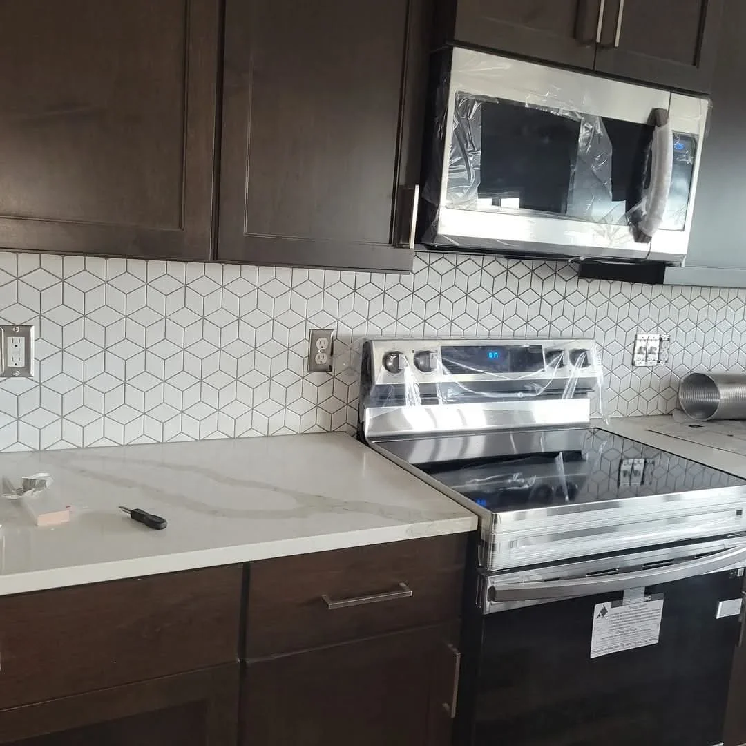 Kitchen with dark cabinets, white quartz counters, geometric hexagon backsplash tile, and stainless steel appliances