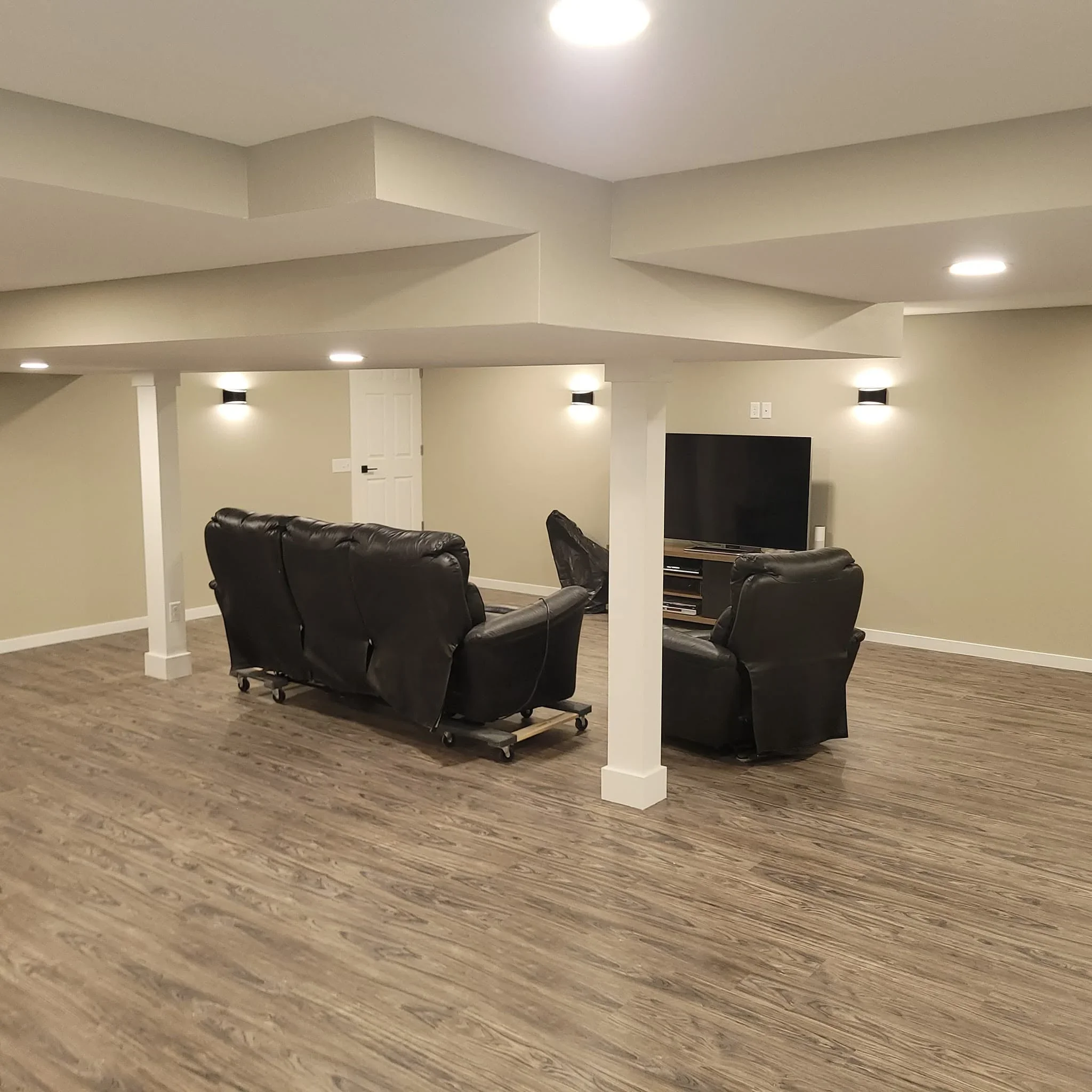 Finished basement with wood flooring, drywall soffit, recessed lights, and white columns