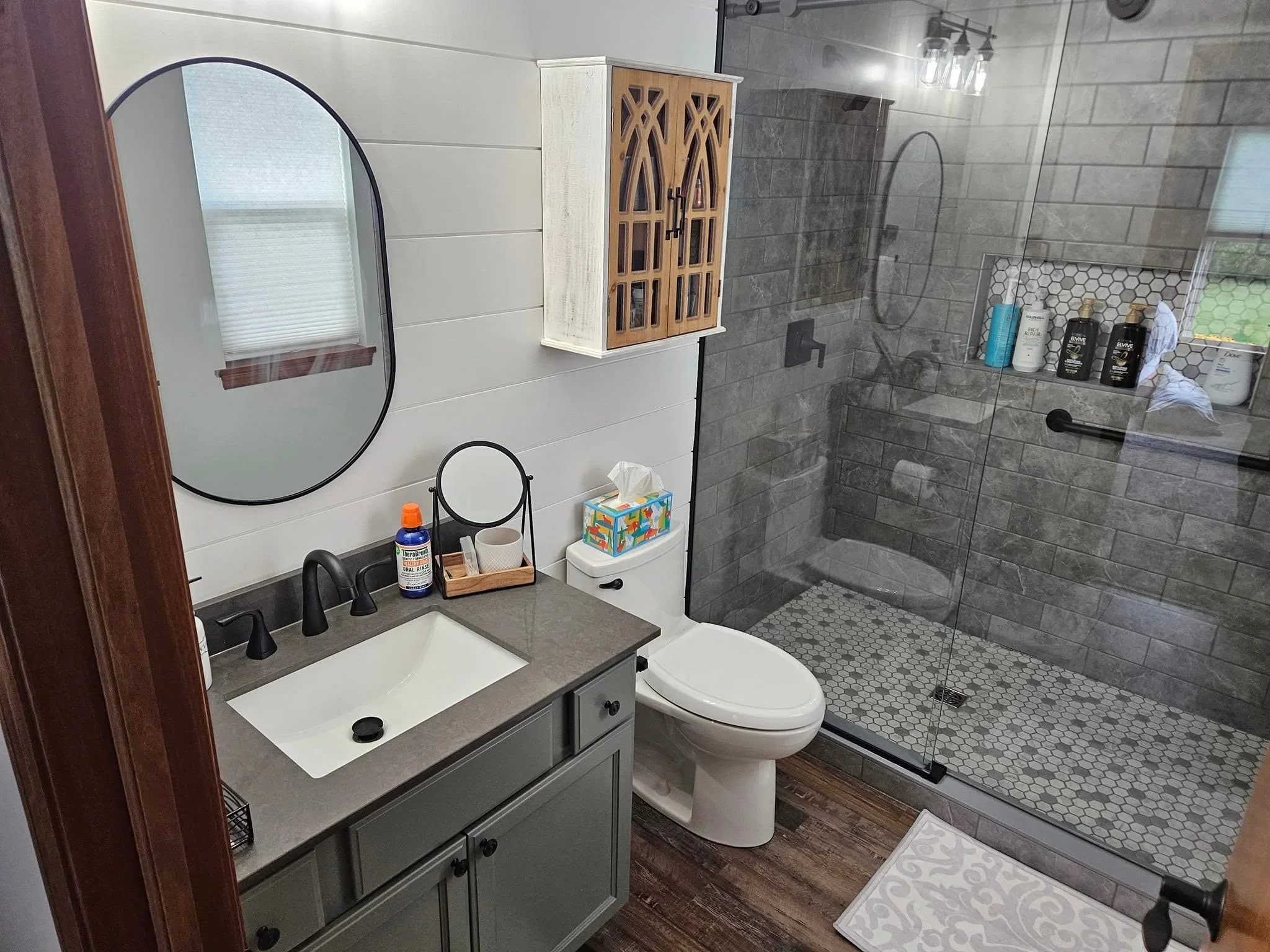 Modern bathroom with gray tile shower, quartz countertop, black fixtures, and shiplap walls