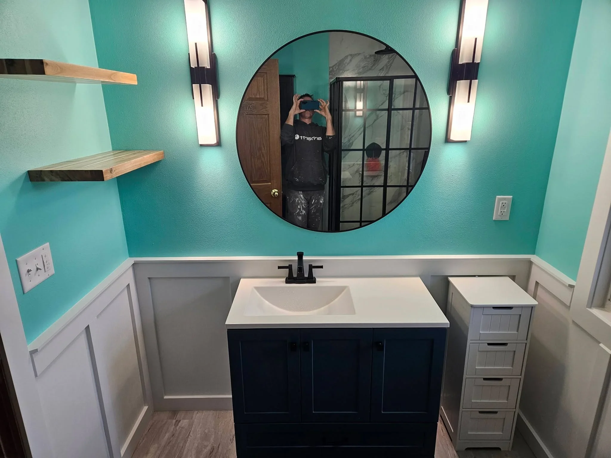 Bathroom vanity with turquoise walls, white wainscoting, black cabinetry, quartz countertop, and circular mirror
