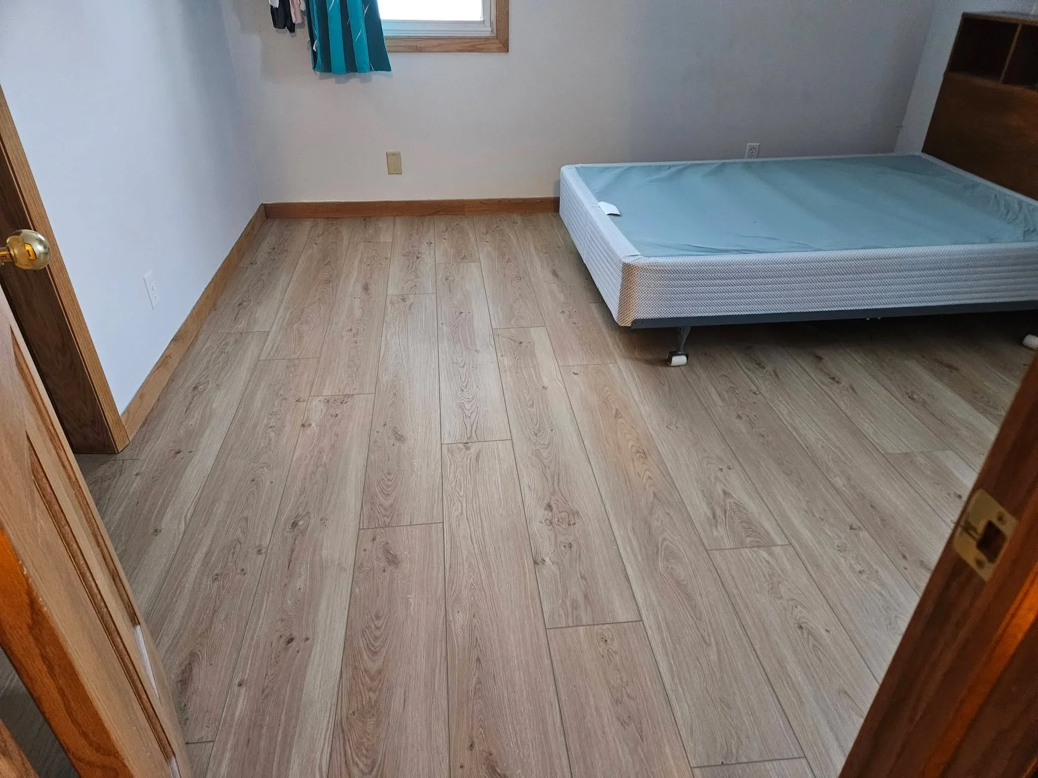 Light gray wood-look vinyl plank flooring installed in bedroom with bed and window visible